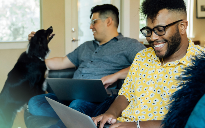 Two happy guys are sitting next to each other and working on their laptops 