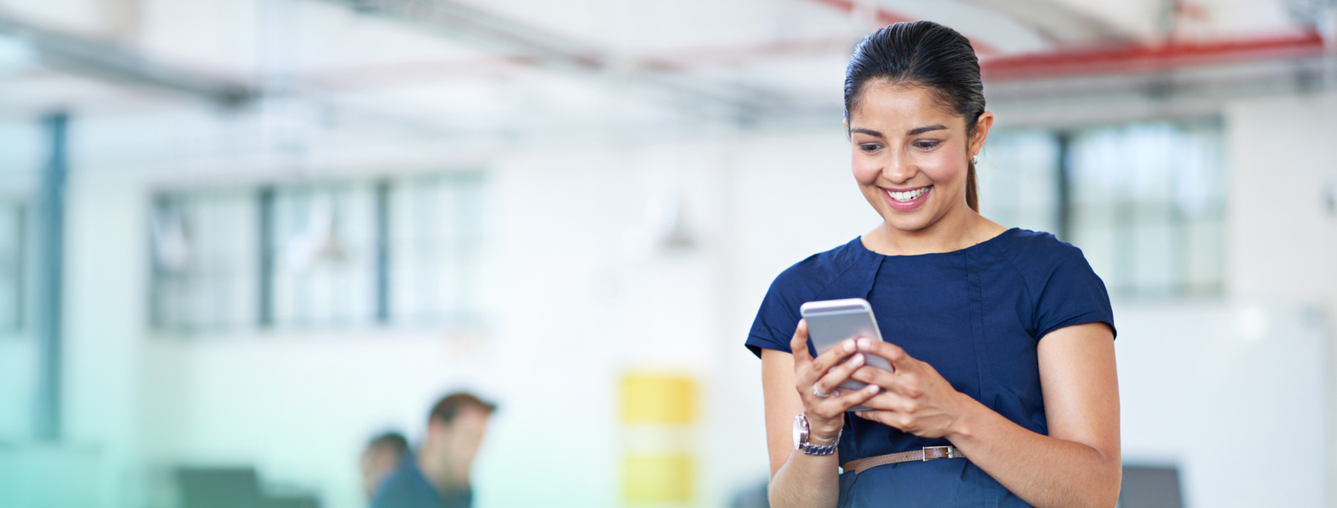 a lady is smiling and holding her phone to learn about employer benefits