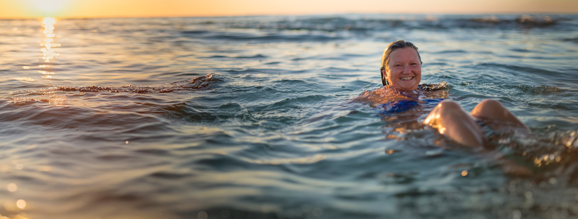 A happy woman lying in the water at the beach during sunset
