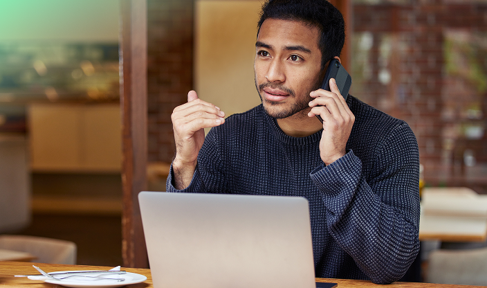 A man sitting in front of the laptop and talking on the phone